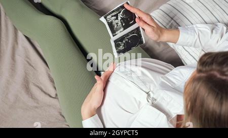 La femme enceinte regarde l'image échographique et fait des courses au ventre Banque D'Images