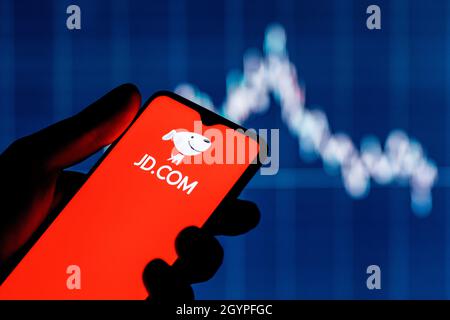 JD.com est une société chinoise de commerce électronique.Un smartphone avec le logo JD.com dans une main.Graphique des actions en arrière-plan. Banque D'Images