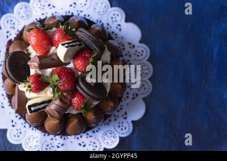 Gros plan d'un gâteau avec des fraises, des biscuits, des truffes au chocolat et du glaçage sur une surface bleue Banque D'Images