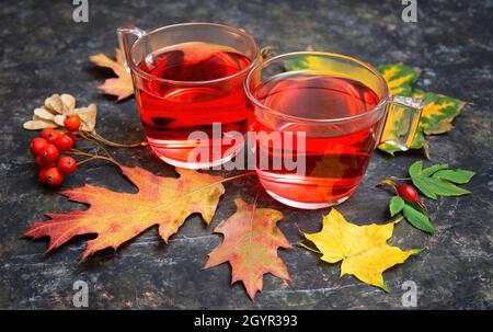 Deux tasses en verre de thé chaud à la grenade avec des feuilles d'automne et des baies vives sur une table ongueuse.La vie tranquille de l'automne. Banque D'Images