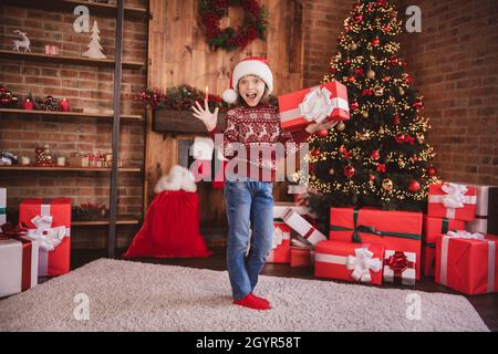 Photo de l'excitée fou choqué impressionné petite fille tenir boîte-cadeau porter chandail santa couvre-tête chaussettes à l'intérieur Banque D'Images