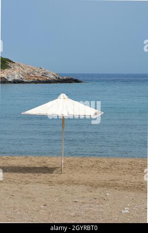 Parasol seul sur la plage à l'île grecque isolée de Sikinos sable, mer et ciel bleu prise de vue verticale avec espace de copie Banque D'Images