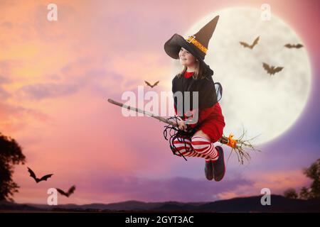 Petit balai volant de sorcière la nuit d'Halloween.Immense pleine lune et chauves-souris en arrière-plan.Costume de jeu ou de cadeau pour enfants.Enfants Amuse-toi bien.Effrayant Banque D'Images