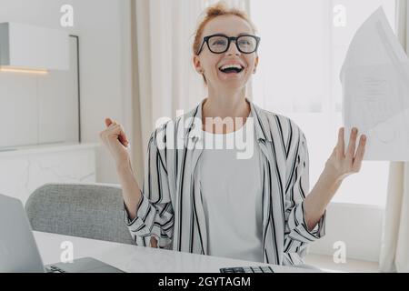 Une jeune femme excitée avec des billets de papier en mains, qui a finalement payé sa dette hypothécaire à la maison Banque D'Images