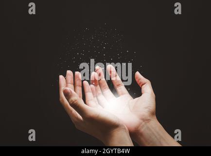 Mains mâles priant avec foi dans la religion pour la bénédiction de Dieu, les lumières croissantes et la poudre magique flottant sur les mains. Banque D'Images