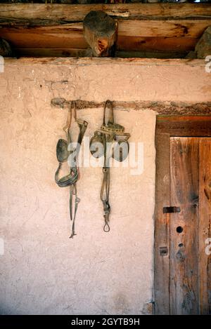 Des œillères anciennes en cuir et d'autres chevaux de tact pendent dans une grange au musée d'histoire vivant El Rancho de las Golondrinas près de Santa Fe, Nouveau-Mexique. Banque D'Images