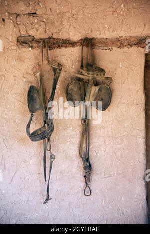 Des œillères anciennes en cuir et d'autres chevaux de tact pendent dans une grange au musée d'histoire vivant El Rancho de las Golondrinas près de Santa Fe, Nouveau-Mexique. Banque D'Images