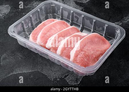 Viande biologique crue.Steaks de porc, filets pour griller, cuire au four ou faire frire ensemble, dans un emballage plastique, sur fond de table noir en pierre foncée, avec copie Banque D'Images