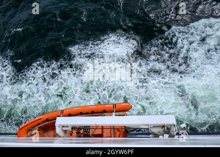 Canot de sauvetage suspendu sur le côté du bateau avec de l'eau mousseuse en dessous. Banque D'Images