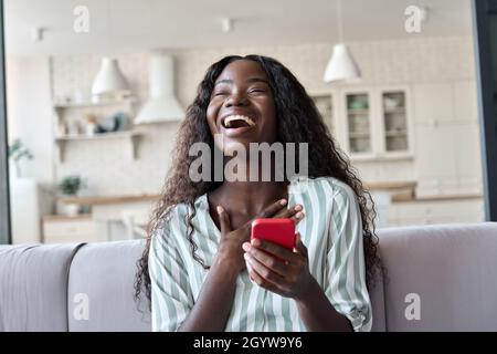 Jeune femme noire excitée tenant le téléphone ressentir la joie d'obtenir le message à la maison. Banque D'Images