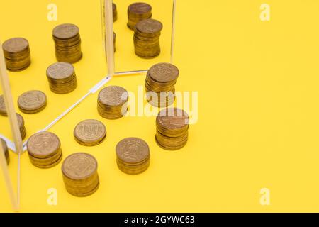 Hryvnia ukrainien en piles. Tours de pièces sur fond jaune près du miroir. Banque D'Images