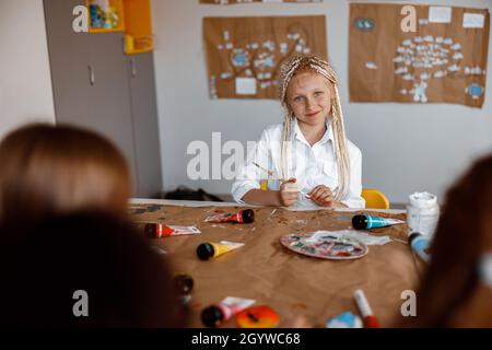 Petite fille mignonne assise à un bureau lors d'une leçon de dessin Banque D'Images