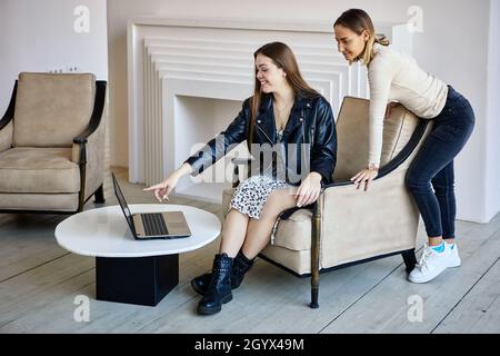 Deux femmes blanches joyeuses travaillent avec un ordinateur portable au bureau. Banque D'Images