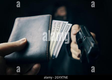 Vol à main armée.La main de l'homme tient le portefeuille d'argent pour voler avec le pistolet.Cent cinquante dollars en porte-monnaie ouvert.L'arme à feu est pointée à la caméra.Criminel dans le capot et le masque.Agression contre un homme non armé. Banque D'Images