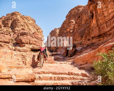 Femme arabe à bord d'un âne sur le sentier Ed-Deir (sentier du monastère) dans l'ancienne ville de Pétra, en Jordanie. Banque D'Images