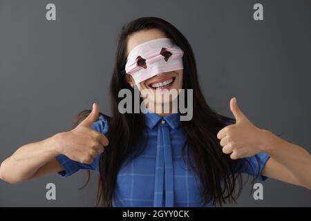 La femme souriante dans le masque sur le visage tient les pouces vers le haut Banque D'Images