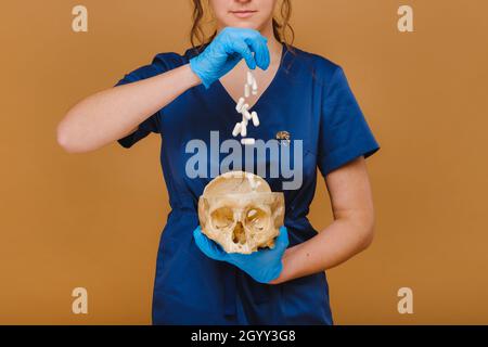 Un jeune médecin verse des capsules de vitamine dans un crâne humain.Le médecin verse des pilules sur le fond Banque D'Images