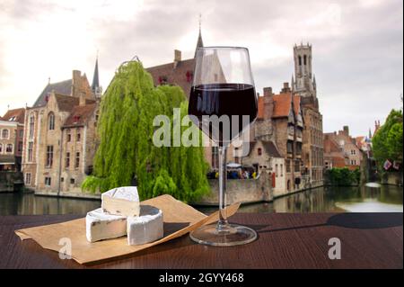 Verre de vin rouge avec en-cas au fromage, vue sur la vieille ville de Bruges et la tour du Beffroi à Bruges, Belgique. Banque D'Images