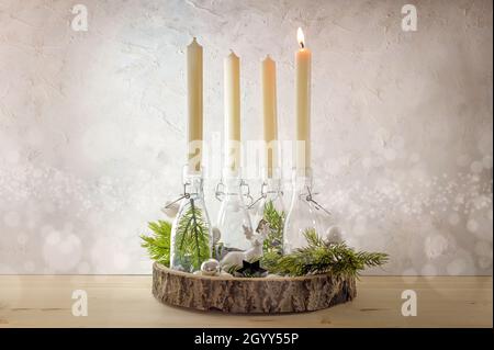 Couronne de l'AVENT créative, bougies en bouteilles sur un panneau en bois avec des branches de sapin et décoration sur un mur rustique léger, on est allumé au premier soleil Banque D'Images