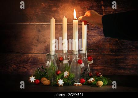 Premier avènement, éclairage à la main une des quatre bougies placées dans des bouteilles avec des branches de sapin et décoration de noël sur un fond rustique en bois sombre, Banque D'Images