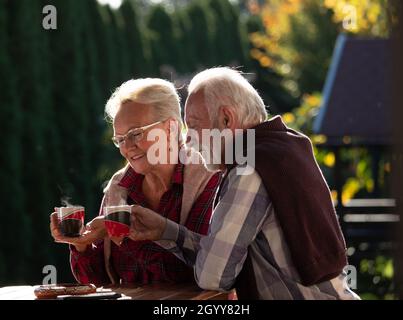 Couple senior romantique assis dans le jardin à table et prenant du café Banque D'Images