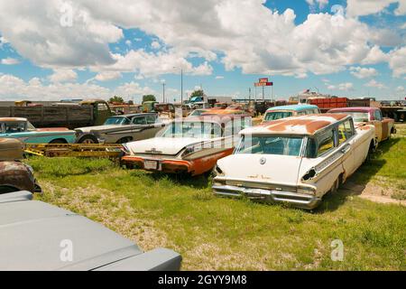 Une collection de voitures classiques vintage garées dans un chantier herbeux sous un ciel bleu éclatant avec des nuages blancs moelleux Banque D'Images
