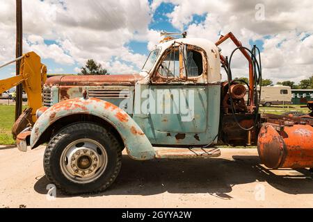 Vieux camion IH de moissonneuse international rouillé avec peinture bleue et blanche garé un jour ensoleillé à côté d'une machine industrielle dans le chantier naval Banque D'Images