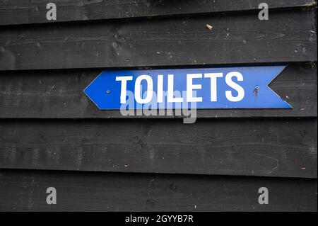 Panneau de toilette bleu et blanc en forme de flèche sur une clôture en bois noir Banque D'Images