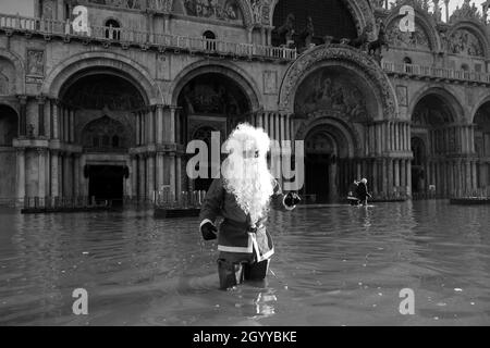 Un homme habillé comme le Père Noël traverse la place Saint-Marc pendant la marée haute à Venise, Italie, le 23 décembre 2019. Banque D'Images