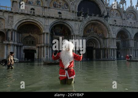 Un homme habillé comme le Père Noël traverse la place Saint-Marc pendant la marée haute à Venise, Italie, le 23 décembre 2019. Banque D'Images