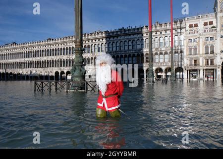 Un homme habillé comme le Père Noël traverse la place Saint-Marc pendant la marée haute à Venise, Italie, le 23 décembre 2019. Banque D'Images