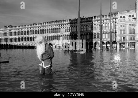 Un homme habillé comme le Père Noël traverse la place Saint-Marc pendant la marée haute à Venise, Italie, le 23 décembre 2019. Banque D'Images