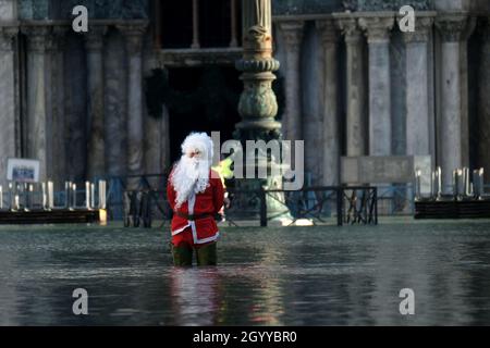 Un homme habillé comme le Père Noël traverse la place Saint-Marc pendant la marée haute à Venise, Italie, le 23 décembre 2019. Banque D'Images