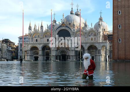 Un homme habillé comme le Père Noël traverse la place Saint-Marc pendant la marée haute à Venise, Italie, le 23 décembre 2019. Banque D'Images