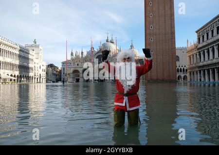 Un homme habillé comme le Père Noël traverse la place Saint-Marc pendant la marée haute à Venise, Italie, le 23 décembre 2019. Banque D'Images