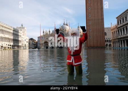 Un homme habillé comme le Père Noël traverse la place Saint-Marc pendant la marée haute à Venise, Italie, le 23 décembre 2019. Banque D'Images