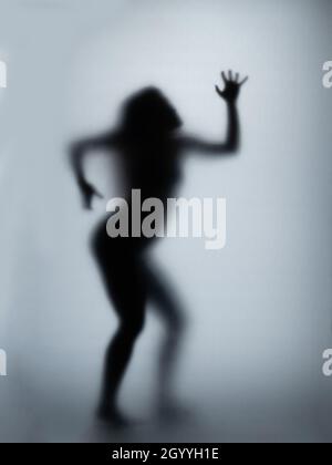 Possédé femme rayant le verre avec les mains, silhouette de femme créepy, horreur.Créature fantôme effrayante derrière le verre. Banque D'Images