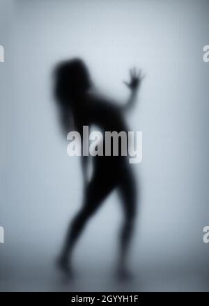 Possédé femme rayant le verre avec les mains, silhouette de femme créepy, horreur.Créature fantôme effrayante derrière le verre. Banque D'Images
