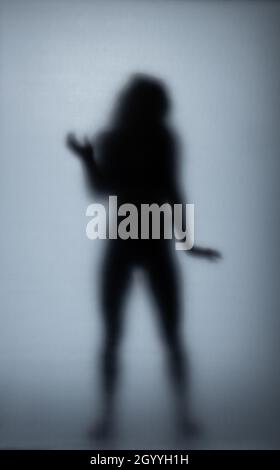 Possédé femme rayant le verre avec les mains, silhouette de femme créepy, horreur.Créature fantôme effrayante derrière le verre. Banque D'Images