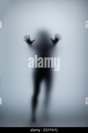 Possédé femme rayant le verre avec les mains, silhouette de femme créepy, horreur.Créature fantôme effrayante derrière le verre. Banque D'Images