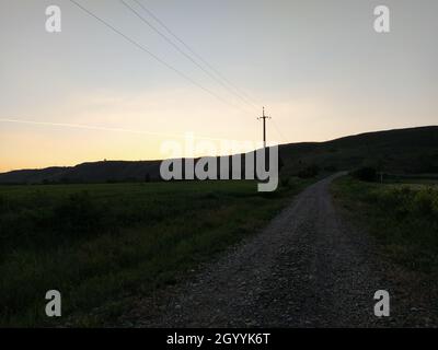 Pôle électrique sous forme de croix au coucher du soleil sur le fond d'une montagne et d'une route Banque D'Images