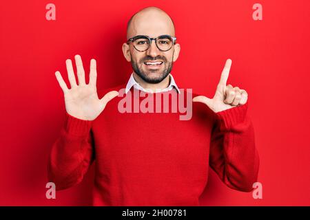 Jeune homme bald portant des vêtements et des lunettes décontractés montrant et pointant vers le haut avec les doigts numéro sept tout en souriant confiant et heureux. Banque D'Images