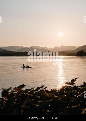 Paddelboarding / Paddleboarders profitant du soleil couchant sur les Langdales lointaines sur le lac Windermere à Low Wood Bay, Lake District Cumbria Angleterre Banque D'Images