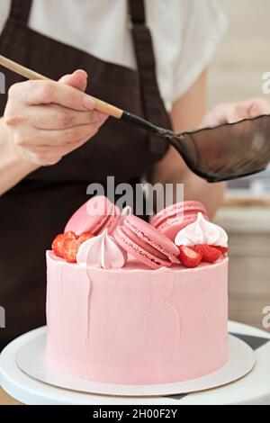 Femme pâtissière décorent le gâteau rose avec des macarons et des baies, gros plan.Processus de fabrication de gâteaux, mise au point sélective Banque D'Images