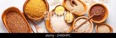 Riz blanc, brun et rouge, sarrasin, millet, gruaux de maïs, quinoa et bulgur dans des bols en bois sur la table de cuisine gris clair. Céréales sans gluten. Haut Banque D'Images