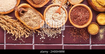 Riz blanc, brun et rouge, sarrasin, millet, gruaux de maïs, quinoa et bulgur dans des bols en bois sur la table de cuisine gris clair. Céréales sans gluten. Haut Banque D'Images