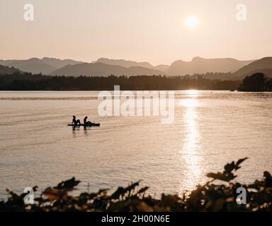 Paddelboarding / Paddleboarders profitant du soleil couchant sur les Langdales lointaines sur le lac Windermere à Low Wood Bay, Lake District Cumbria Angleterre Banque D'Images