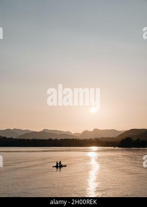 Paddelboarding / Paddleboarders profitant du soleil couchant sur les Langdales lointaines sur le lac Windermere à Low Wood Bay, Lake District Cumbria Angleterre Banque D'Images