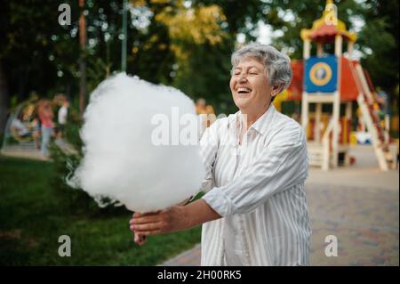 La granny souriante tient des bonbons en coton, parc d'attractions Banque D'Images