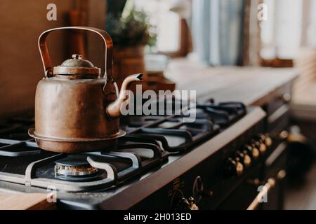 Une vieille bouilloire en aluminium s'enbouilant sur une cuisinière à gaz dans la cuisine sur un arrière-plan confortable et flou.Objet ancien en cuivre.Style vintage Banque D'Images